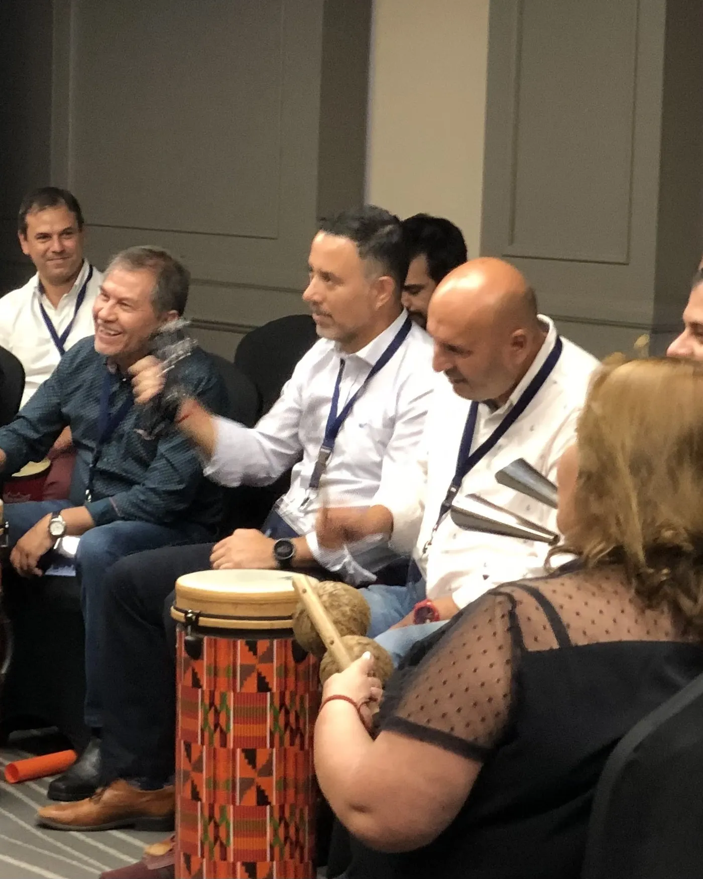 Colegas sonriendo y riendo mientras tocan tambores y percusión durante una experiencia de equipo.