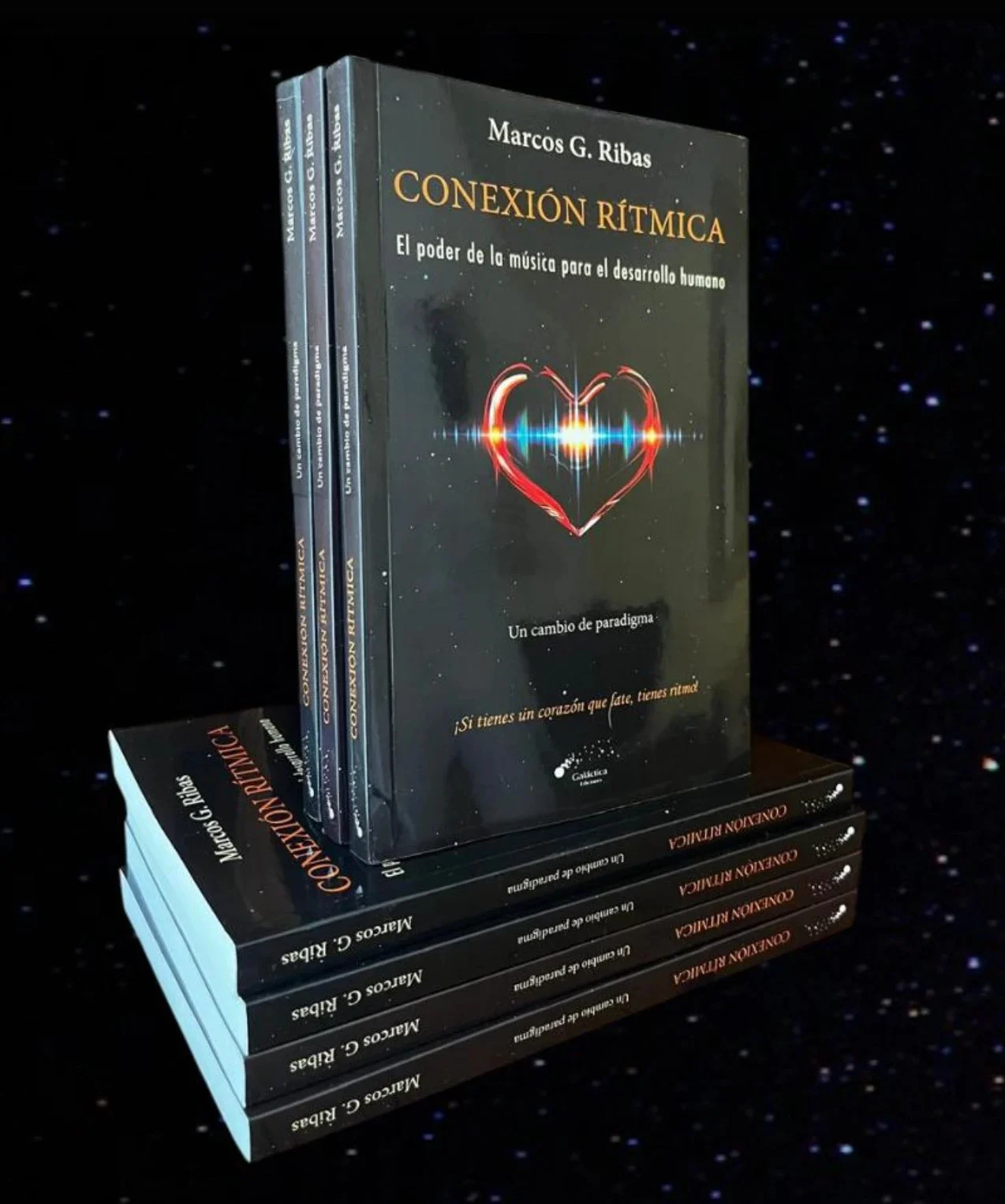 Pila de ejemplares del libro Conexión Rítmica, de Marcos G. Ribas: tres de pie, con la portada de un corazón de luz, y cuatro apilados, con el lomo a la vista.